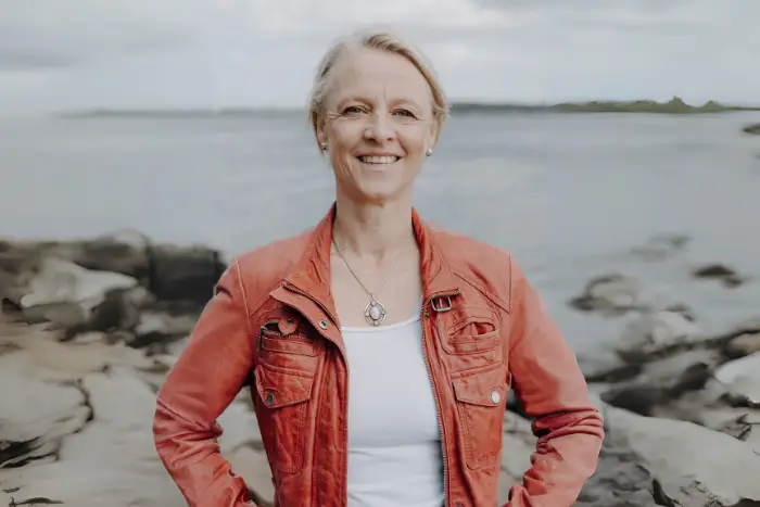 Dr. Tenna Dahl stellt sich lächelnd vor. Im Hintergrund sieht man das Meer und die Küste.