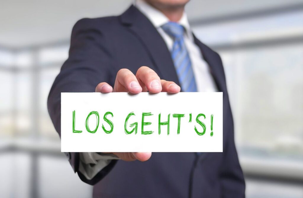 Verschwommener Geschäftsmann hält ein Schild mit der Aufschrift ‚LOS GEHT’S!‘ nach vorne, Symbol für Generative AI Optimization und den Start von Projekten.
